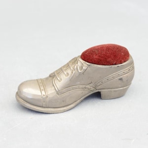 Peut inclure: Un coussin à épingles en forme de chaussure argentée avec un dessus en velours rouge. La chaussure présente des coutures détaillées et un petit talon. Un accessoire de couture unique.