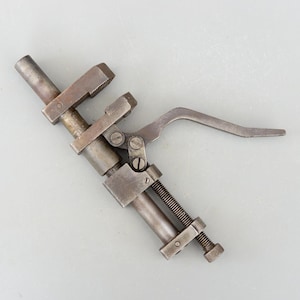 Könnte beinhalten: Ein Vintage-Werkzeug aus Metall mit einem Griff und einer Gewindestange. Das Werkzeug hat einen klemmartigen Mechanismus mit einer gezahnten Backe.