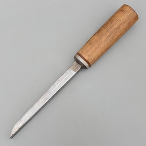 May include: A chisel with a wooden handle and a metal blade. The handle is light brown, and the blade is silver. The chisel is designed for woodworking and has a sharp, angled tip.