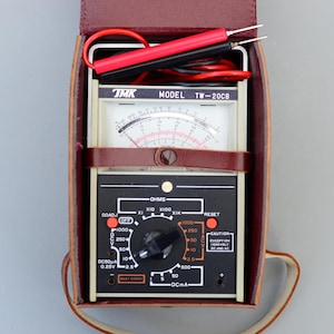 May include: A vintage TMK TW-20CB analogue multimeter in a brown leather case with red and black test leads. The multimeter has a dial with a needle and a variety of settings, including ohms, DC volts, and DC amps.