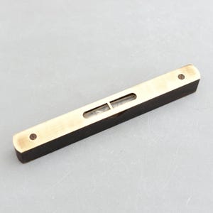 May include: A brass spirit level with a black wooden base. The level has a glass vial with a bubble to indicate when a surface is level.