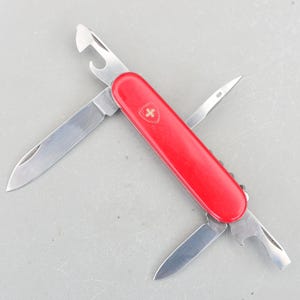 May include: A red Swiss Army knife with a variety of tools, including a blade, a bottle opener, a can opener, and a screwdriver.