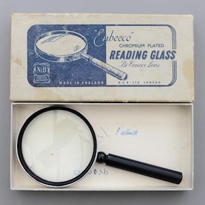 以下が含まれることがあります： オリジナルボックスに入った、ビンテージの「Enbeeco」クロムメッキ読書用ルーペ。凸レンズ付き。拡大鏡は黒いハンドルとシルバーフレームです。箱は薄い青と白で、テキストが書かれています。