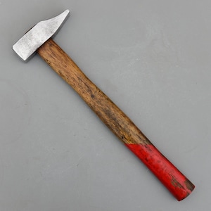 May include: A claw hammer with a wooden handle and a silver metal head. The handle is stained brown with a red painted end. The hammer is designed for driving nails and other fastening tasks.