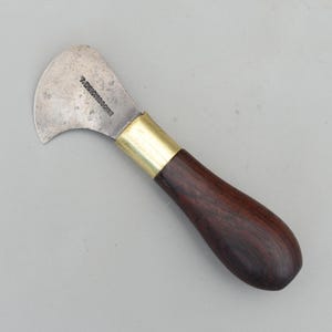 Peut inclure: Un couteau ancien à lame incurvée avec un manche en bois foncé et une virole en laiton. La lame argentée porte l'inscription "T. DICKINSON & SONS". Le couteau est conçu pour un usage spécifique.