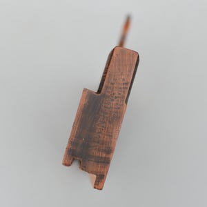 May include: A close-up of a wooden tool with a dark brown finish. The tool has a rectangular body with a notch and a handle. The wood grain is visible, and there is text etched into the surface.