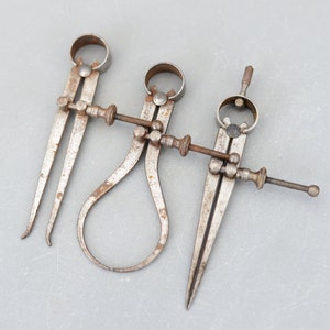 Puede incluir: Un juego de tres calibradores de metal vintage con un acabado oxidado. Los calibradores se utilizan para medir el diámetro de los objetos.