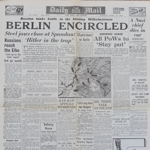 Peut inclure: Une page de journal d'époque du 24 avril 1945, avec des titres sur la bataille de Berlin. Le texte comprend des phrases comme "Berlin encerclée" et "Hitler dans le piège". Le journal est jauni par le temps.