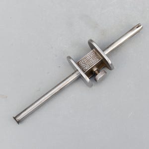 May include: A vintage Stanley No. 97 marking gauge, made of silver-colored metal. The tool has a sliding head with a screw for adjustment and two round guides. The Stanley logo and "No. 97" are visible on the head.