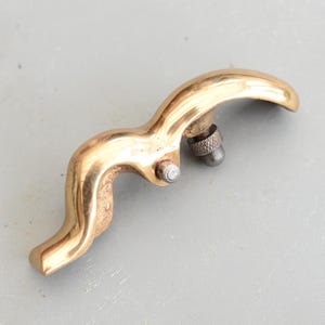 May include: A brass hand plane tool with a curved handle and a small adjustment knob. The tool is used for smoothing wood.