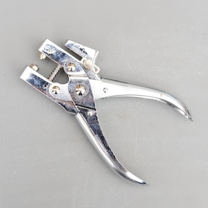 May include: A silver metal tool with a handle and a lever. The tool is used for punching holes in materials.