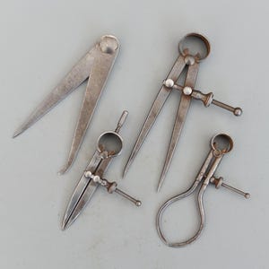 Może przedstawiać: Cztery różne rodzaje metalowych suwmiarki, w tym suwmiarka wewnętrzna, suwmiarka zewnętrzna i dwie pary cyrkli.