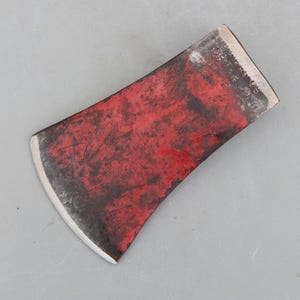 May include: A vintage axe head with a red painted surface and a sharp, curved blade. The axe head has visible wear and tear, with the word "OREGON" stamped on the top edge. The axe head is designed for chopping wood.