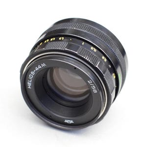 May include: A black Helios-44M 2/58 lens with a silver ring around the lens barrel. The lens has a black lens cap and a silver aperture ring.