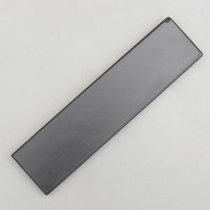 Peut inclure: Un objet rectangulaire de couleur gris foncé avec une surface lisse. L'objet est long et étroit, avec un bord légèrement biseauté. Il semble être fait d'un matériau solide, peut-être de la pierre ou du métal.