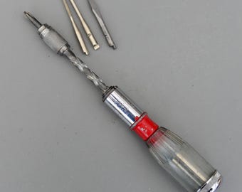 May include: A vintage screwdriver set with a clear plastic handle, red accent, and silver metal components. The set includes the main screwdriver and several interchangeable bits. The handle is approximately 6 inches long.