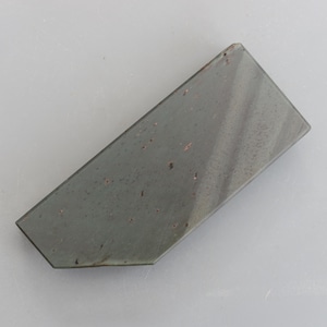 May include: A dark grey sharpening stone with a rough, textured surface. The stone has a slightly irregular shape and is made of natural materials.