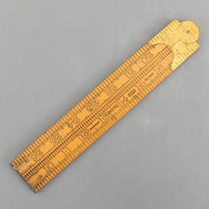 May include: A vintage wooden folding ruler, with black markings and numbers. The ruler is made of boxwood and has a brass hinge. The ruler is approximately 66 cm long when fully extended.