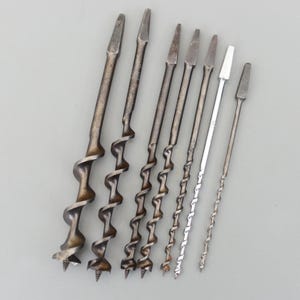 Może przedstawiać: Kolekcja antycznych wierteł świdrowych, o różnych rozmiarach i wzorach. Wiertła metalowe mają spiralną konstrukcję do usuwania materiału. Kolekcja obejmuje wiertła o różnych długościach i szerokościach, prezentując gamę narzędzi do obróbki drewna.