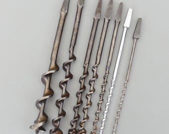 Peut inclure: Une collection d'anciennes mèches de tarière, de tailles et de modèles variés. Les mèches métalliques présentent un design en spirale pour l'extraction de matière. La collection comprend des mèches de différentes longueurs et largeurs, présentant une gamme d'outils de menuiserie.