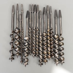 May include: A collection of vintage auger drill bits, arranged in a row. The bits are made of metal, with a spiral design and pointed tips. The drill bits vary in size and shape, suitable for woodworking or construction projects.