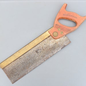 Pode incluir: Uma serra de mão vintage Spear & Jackson com uma lâmina de latão e uma pega de madeira. A pega é pintada de laranja e tem um botão de latão.