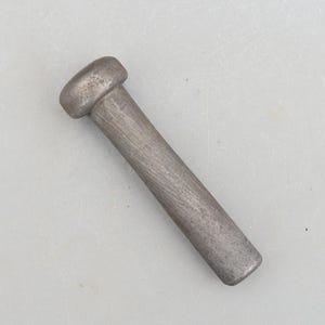 Op de afbeelding: Een grijze metalen staaf met een afgeronde bovenkant. De staaf heeft een getextureerd oppervlak.