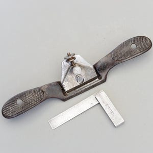 Puede incluir: Un cepillo de mano de metal vintage con un mango de goma negro y una escuadra de metal. La escuadra está marcada con "Stanley No. 45"