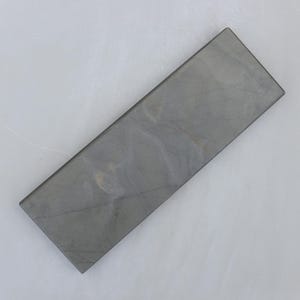 May include: A rectangular sharpening stone with a gray, marbled appearance. The stone has a smooth surface and is designed for sharpening knives and other tools. The stone is approximately 8 inches long and 2 inches wide.