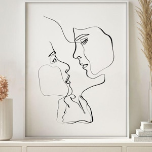 May include: Black and white line art print of two faces in profile, nearly touching. The minimalist artwork is framed in a white border, creating a modern aesthetic. The artwork is displayed on a white cabinet, with decorative elements in the background.