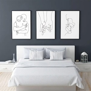 May include: Three framed black and white line art prints depicting human figures. The art pieces are displayed above a bed with white bedding and decorative pillows. The wall behind the art is a dark gray color.