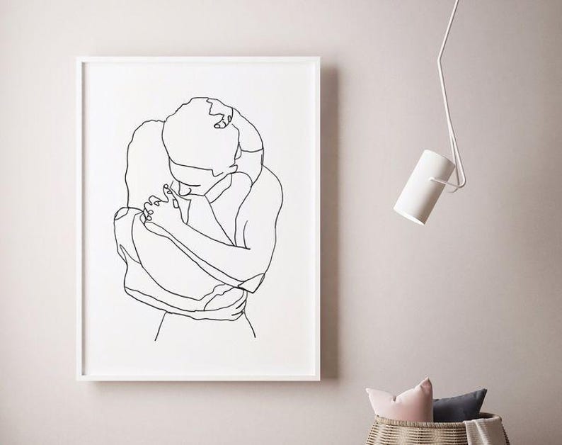 May include: A framed black and white line art print depicting two figures embracing. The artwork is minimalist, with a focus on the outlines of the figures. The print is displayed on a light-colored wall, with a white frame.