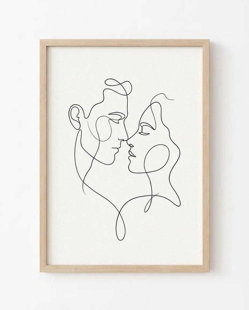 May include: A framed minimalist line art print featuring two faces in profile, almost touching. The black lines create the outlines of a man and a woman, set against a white background. The artwork is in a light-colored wooden frame.