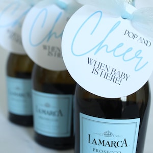 Könnte beinhalten: Drei Mini-Flaschen LaMarca Prosecco-Sekt mit blauen und weißen runden Etiketten, auf denen "Pop and Cheer When Baby is Here!" steht.