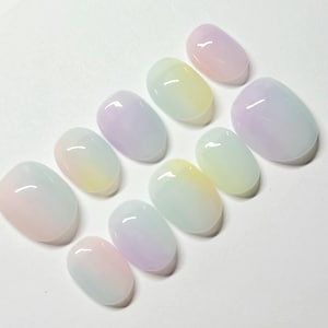 May include: A set of ten oval-shaped artificial nails. Each nail features a gradient design with pastel colors, including pink, yellow, blue, and purple. The nails have a glossy finish, reflecting light.