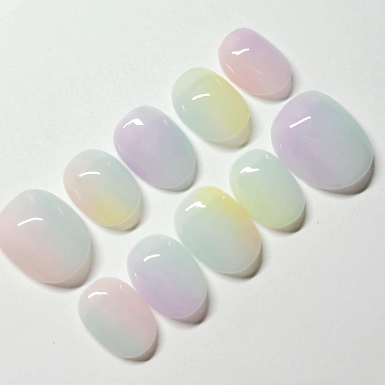 K&ouml;nnte beinhalten: Ein Set aus zehn oval geformten Kunstn&auml;geln. Jeder Nagel zeigt ein Farbverlaufsdesign mit Pastellfarben, darunter Rosa, Gelb, Blau und Lila. Die N&auml;gel haben ein gl&auml;nzendes Finish und reflektieren das Licht.