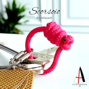 Könnte beinhalten: Ein leuchtend rosa Schlüsselband aus Seil mit einem Knoten in Form einer Acht. Das Schlüsselband ist an einem Schlüsselsatz mit einem goldfarbenen Schlüsselanhänger befestigt.