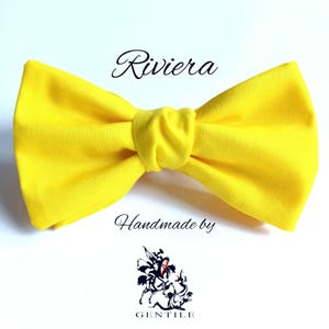 Puede incluir: Una pajarita de color amarillo brillante con el texto "Riviera" encima y "Handmade by Gentile" debajo.