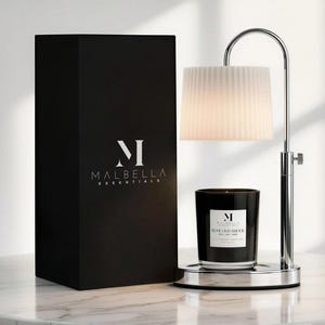May include: A black box with the Malbella Essentials logo next to a candle warmer with a white lampshade and a black candle. The candle has a label that reads "Rose Oud Amour".