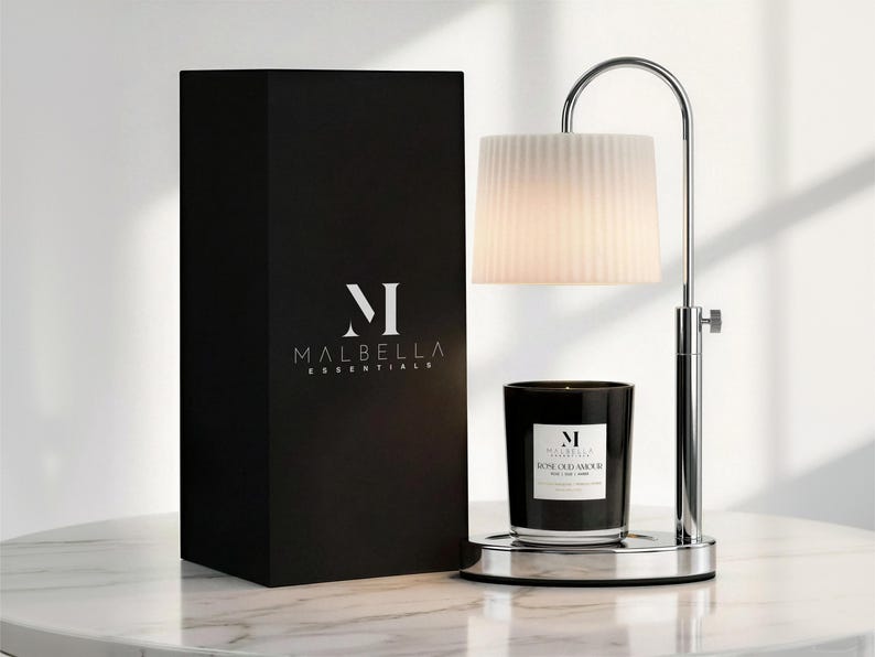May include: A black box with the Malbella Essentials logo next to a candle warmer with a white lampshade and a black candle. The candle has a label that reads "Rose Oud Amour".