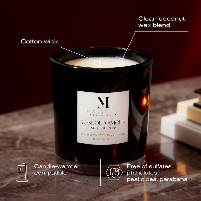 May include: A black glass candle with a white label that reads "ROSE OUD AMOUR". The candle has a cotton wick and a clean coconut wax blend. It is candle-warmer compatible and free of sulfates, phthalates, pesticides, and parabens. The net weight is 240g / 8.5oz.
