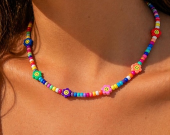 May include: A colorful beaded necklace with a rainbow of small beads. The necklace features several flower-shaped beads with smiley faces. The necklace is worn around the neck.