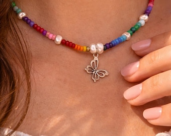 May include: A colorful beaded necklace with a silver butterfly pendant. The necklace features a rainbow of beads and freshwater pearls. The butterfly pendant is a delicate, openwork design. The necklace is a stylish accessory.