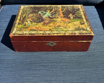 May include: A rectangular wooden box with a hinged lid. The lid features a colorful painting of figures in a forest scene. The box has a dark brown finish and a small keyhole on the front.