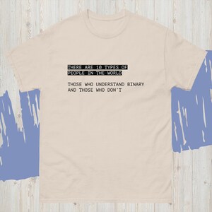 May include: A beige t-shirt with black text. The text reads: "THERE ARE 10 TYPES OF PEOPLE IN THE WORLD. THOSE WHO UNDERSTAND BINARY AND THOSE WHO DON'T."