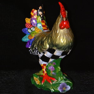 May include: A ceramic rooster figurine featuring a gold-toned neck, a bright red comb and wattle, and a tail with multicolored patterned feathers. The body displays a black and white checkered pattern, while the base is green with floral accents.