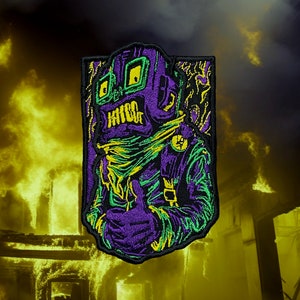 May include: Purple and green embroidered patch of a robot with a yellow bandana and goggles. The robot is giving a thumbs up. The patch is set against a background of yellow flames.