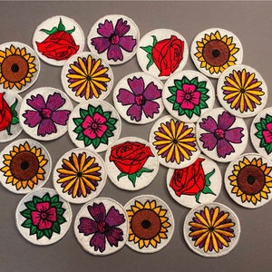May include: A collection of 20 embroidered iron-on patches featuring various floral and sunflower designs. The patches are circular and have a white background with colourful embroidery.