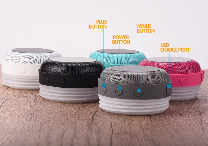 May include: Four portable Bluetooth speakers in different colors: white, black, gray, and pink. Each speaker has a USB charging port, power button, plus and minus buttons, and a textured top.
