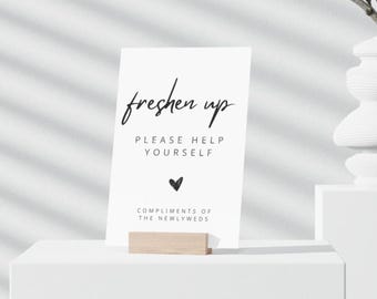 May include: White card with black text that reads "freshen up" and "Please help yourself". A small black heart is below the text. The text "Compliments of the newlyweds" is at the bottom of the card.